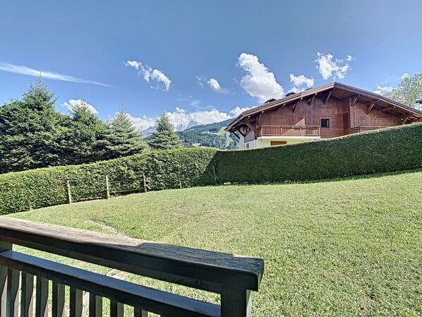 A wooden chalet with a sloped roof, surrounded by a well-maintained hedge and a grassy field. - Charming 2-room apt in Combloux with terrace, parking and ski locker (Combloux)