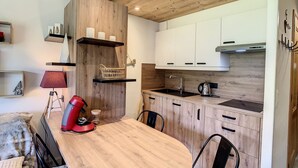 A modern kitchen with wooden cabinets, a built-in stove, and a dining table with chairs. - Charming 2-room apt in Combloux with terrace, parking and ski locker (Combloux)