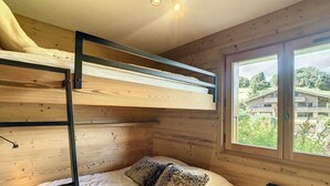 A bunk bed with a wooden headboard, a window with a view of buildings, and a radiator. - Charming 2-room apt in Combloux with terrace, parking and ski locker (Combloux)