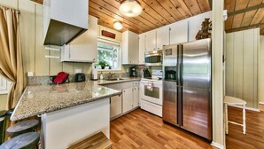 A kitchen with wooden flooring, white cabinets, a stainless steel refrigerator, and a granite countertop. - Cozy Forest Getaway | Foosball Fun + A/C Comfort (South Lake Tahoe)