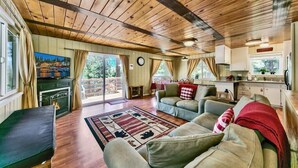 A spacious living area with a wooden ceiling, a fireplace, a sofa set, and a kitchen area. - Cozy Forest Getaway | Foosball Fun + A/C Comfort (South Lake Tahoe)