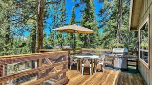 A wooden deck with a grill and outdoor seating area, surrounded by tall trees. - Cozy Forest Getaway | Foosball Fun + A/C Comfort (South Lake Tahoe)