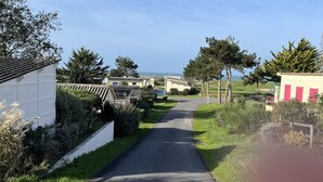 A narrow road flanked by greenery and buildings, leading towards a distant view. - Sea view bungalow (Coudeville-sur-Mer)