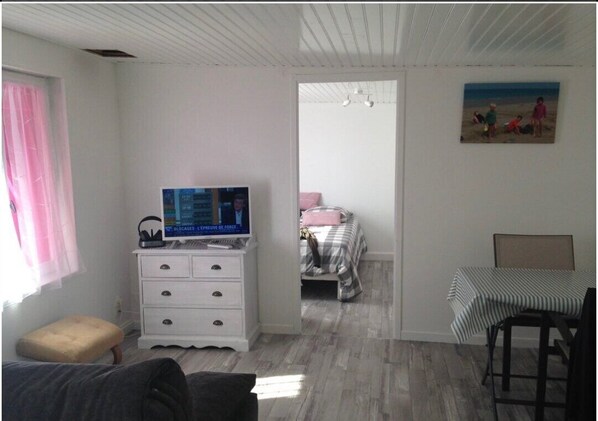 A bedroom with a bed, a dresser with a TV, a window with curtains, and a painting on the wall.