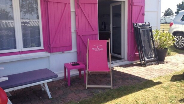 A building with pink shutters, a bench, a small table, and a chair outside. - Sea view bungalow (Coudeville-sur-Mer)