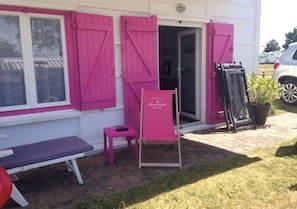 A building with pink shutters, a bench, a small table, and a chair outside.