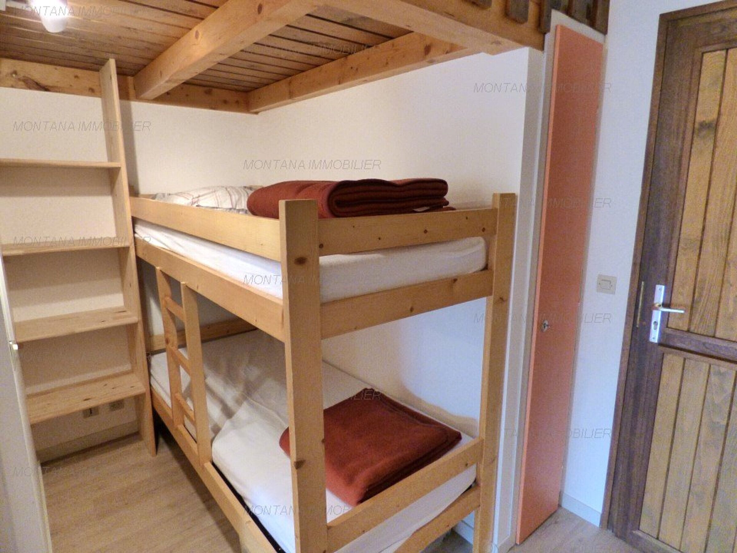 Habitación con literas, vigas de madera, una puerta y una pared blanca con un sello de agua.