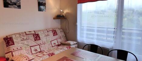 A cozy room with a patterned sofa, a wooden table with menus, and a window with curtains.