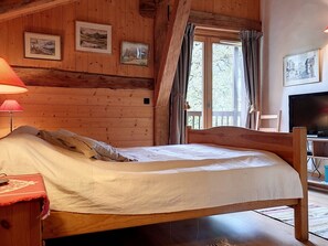 A wooden cabin bedroom with a bed, a lamp, a TV, and framed pictures on the wall. - Renovated 3-star chalet, 14 people, Mont Blanc view, Wifi (Cordon)