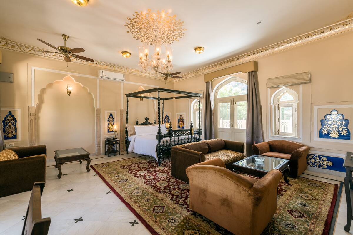Ein geräumiges Zimmer mit einem großen Bett, einer Sitzecke mit Sofas, einem Glastisch und einem Chandelier.
