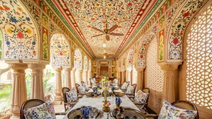 A dining area with ornate ceiling and walls, a ceiling fan, and a long table set for a meal. - Mundota Fort and Palace (Jalsu)