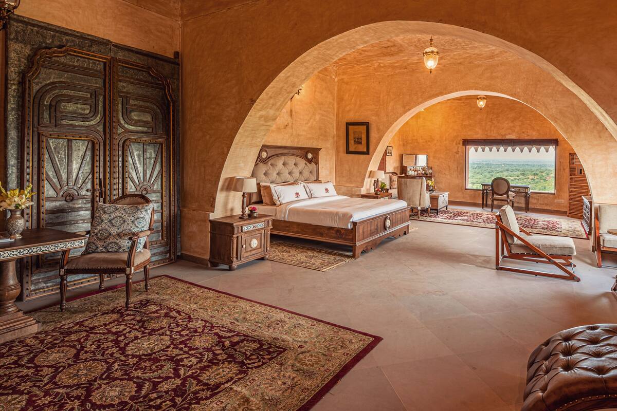Ein geräumiges Schlafzimmer mit einem großen Bett, einem Holzschrank, einem Schreibtisch und Blick auf die Landschaft durch ein Rundbogenfenster.