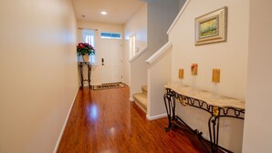 A hallway with wooden flooring, a white door, a staircase, and a console table with candles. - Tacoma House INN W/ Centralized AC (Tacoma)