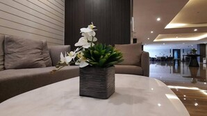 A modern lobby with a sofa, a round table with a potted plant, and a dark wooden wall.