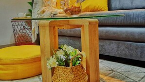 A living room with a sofa, cushions, a small wooden table with a glass top, and a woven basket with flowers.