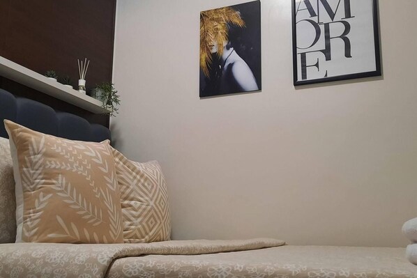 A bedroom with a bed, a pillow, a wall-mounted shelf with decorative items, and two framed pictures.