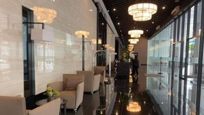 A modern hotel lobby with a long corridor, seating area with sofas, and large windows.