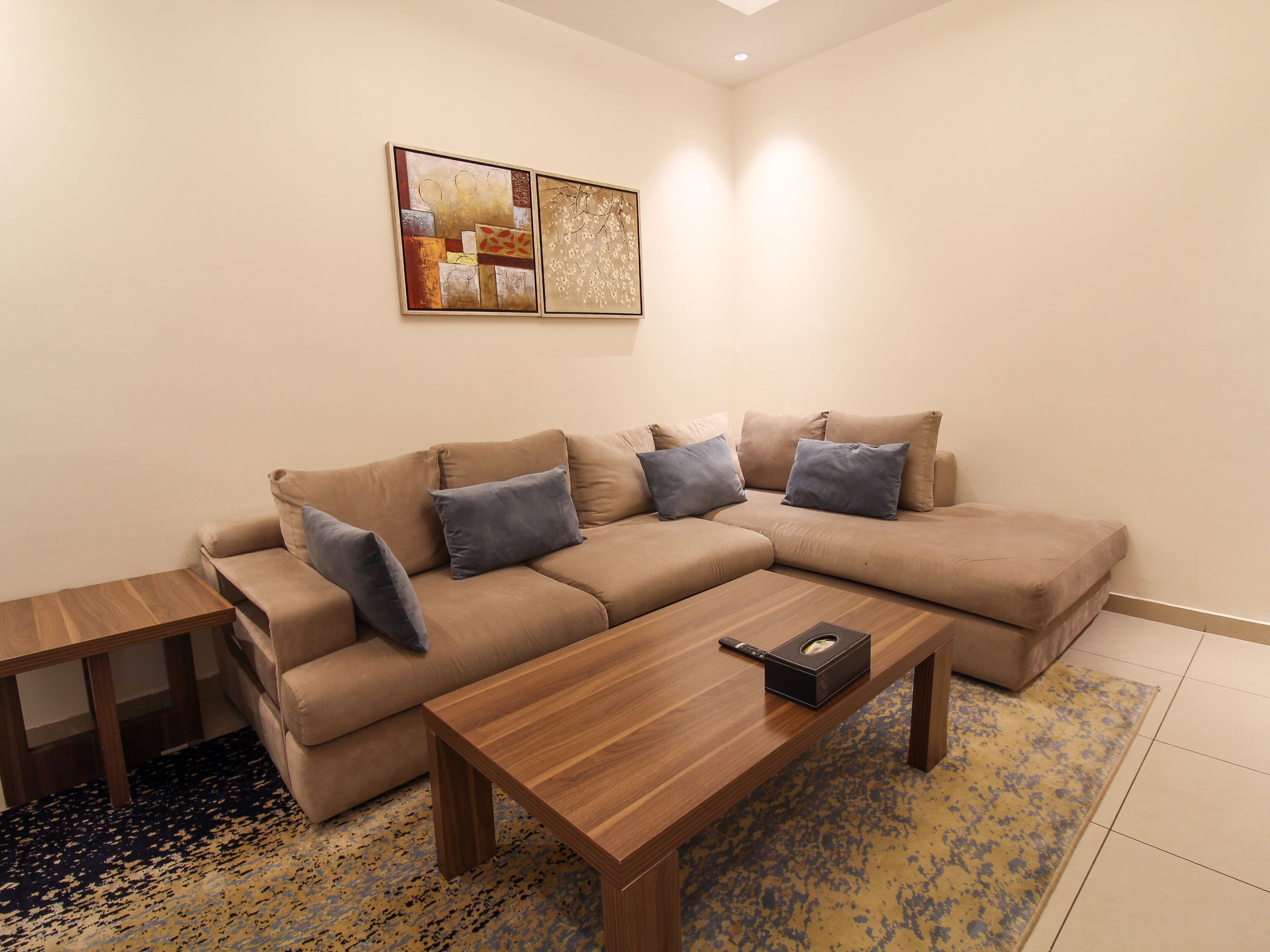 A living room with a beige sectional sofa, two wooden coffee tables, and a patterned rug.