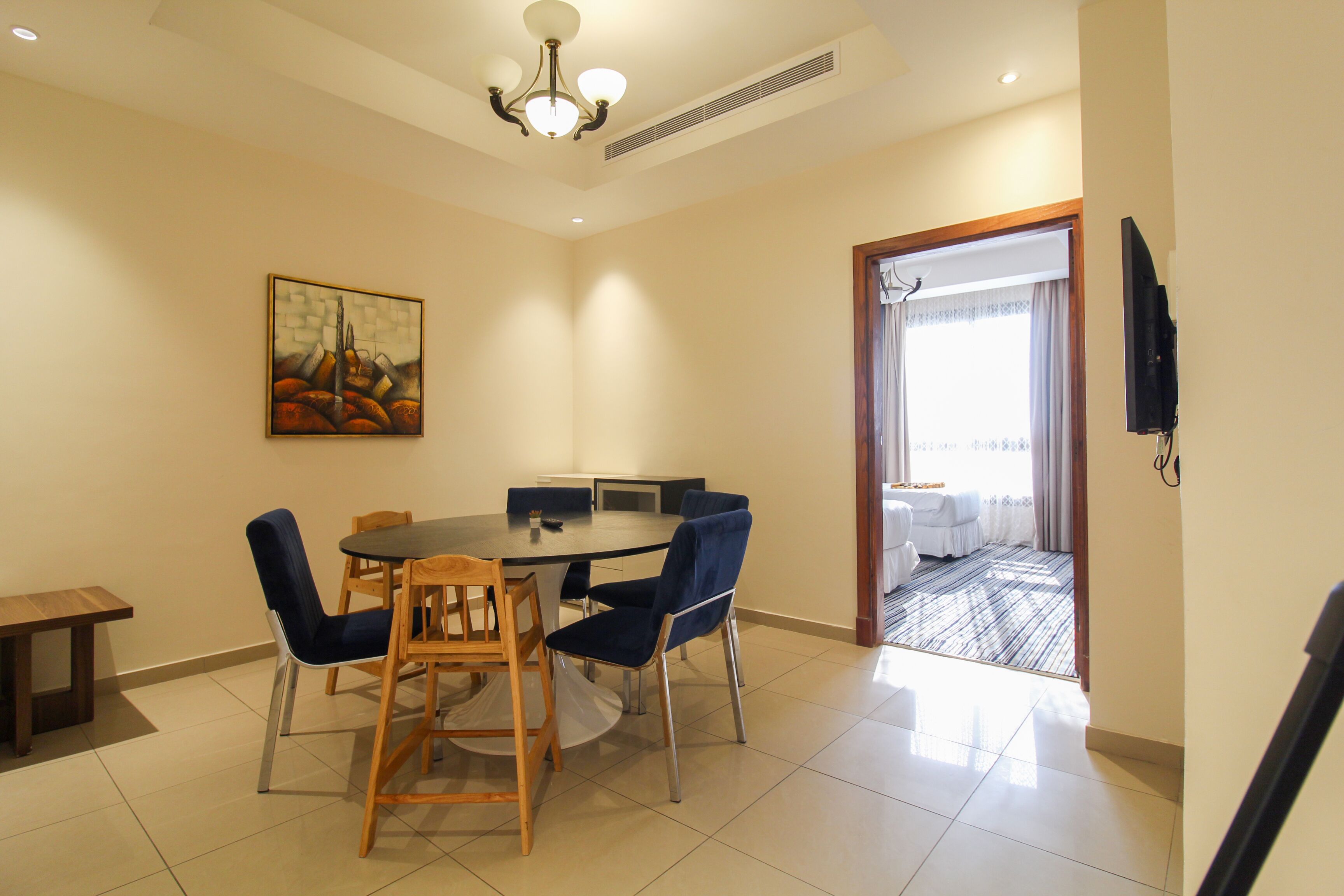A dining area with a round table, blue chairs, and a painting on the wall.