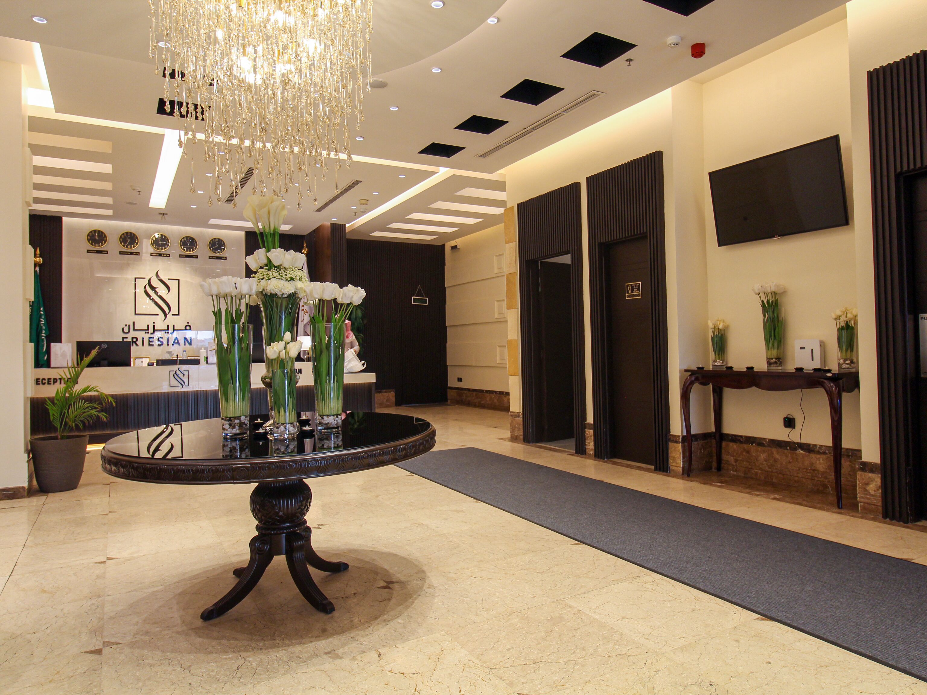 A reception area with a round table, vases of flowers, a chandelier, and a reception desk with a sign.