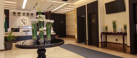 A reception area with a round table, vases of flowers, a chandelier, and a reception desk with a sign.