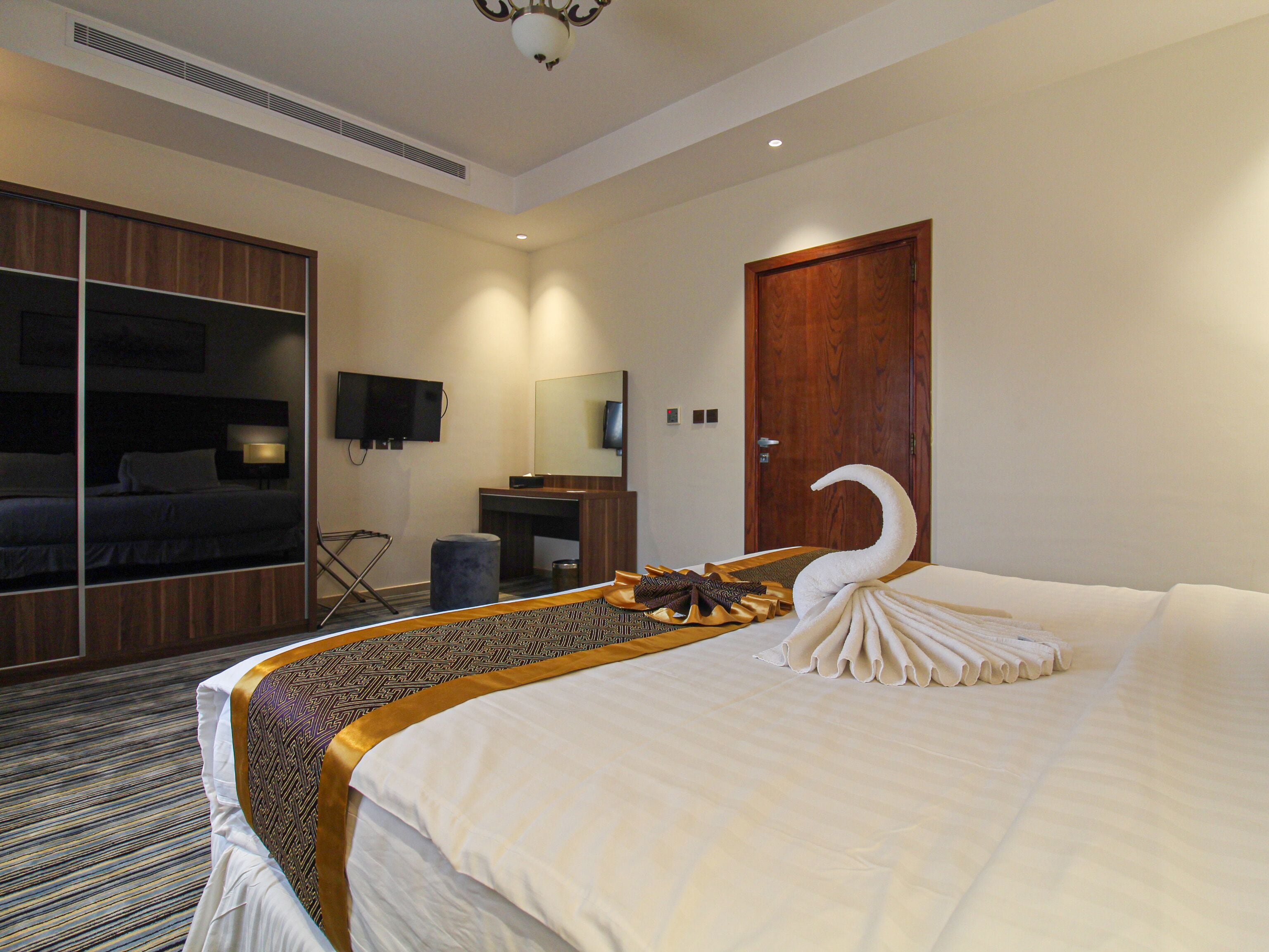 Une chambre d’hôtel avec un grand lit, une armoire en bois, un bureau avec un miroir, une télévision et une porte.