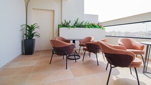 A balcony with a table and chairs, a potted plant, and a view of buildings. - Freisian for Hotel Apartment (Jeddah)