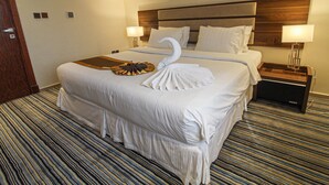 A hotel room with a large bed, two bedside tables, a headboard, and a painting on the wall. - Freisian for Hotel Apartment (Jeddah)