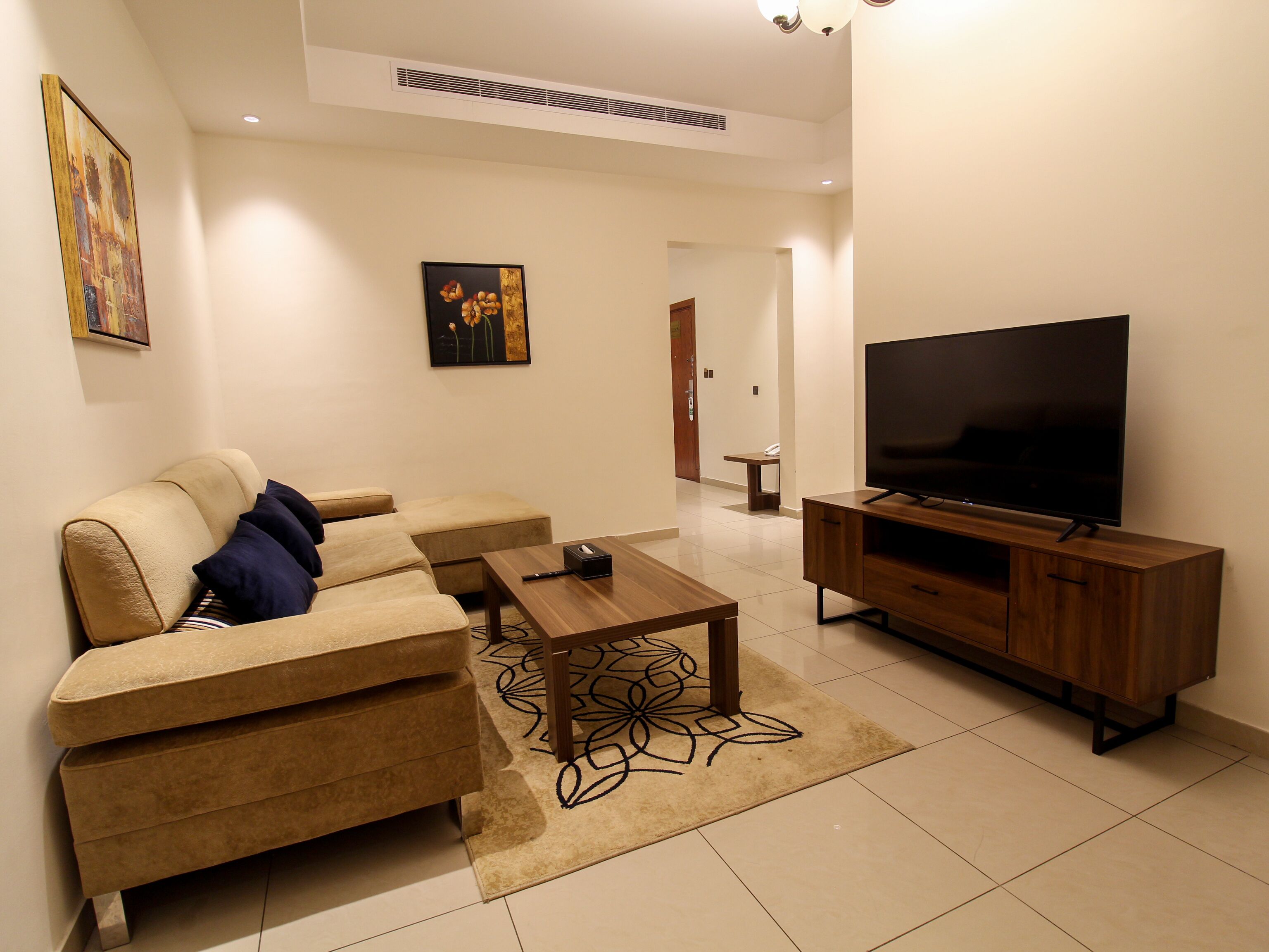 A modern living room with a sectional sofa, a coffee table, a TV on a wooden stand, and artwork on the walls.