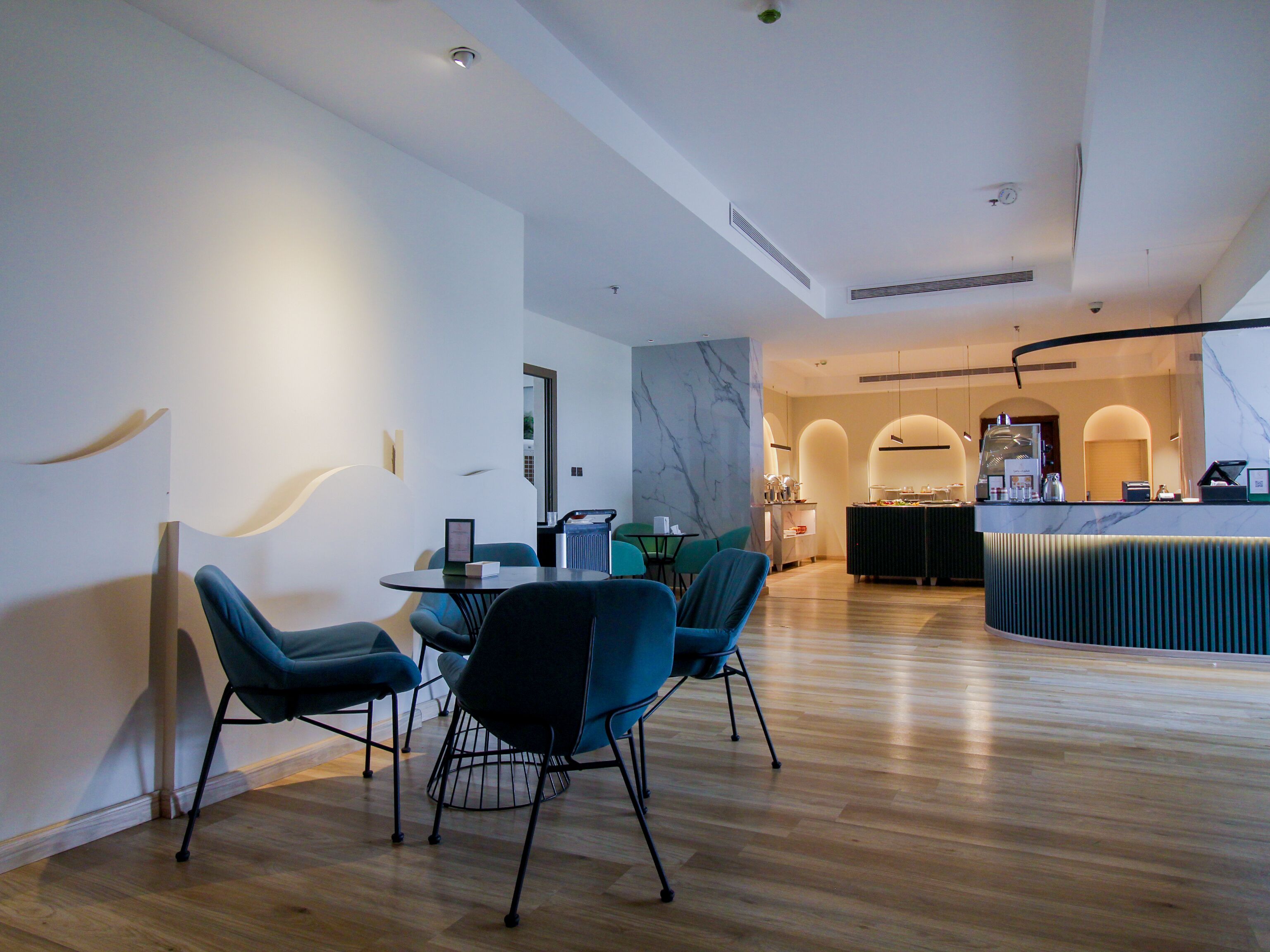 En moderne hotellobby med trægulv, receptionsdisk og spiseområde med blå stole og et bord.
