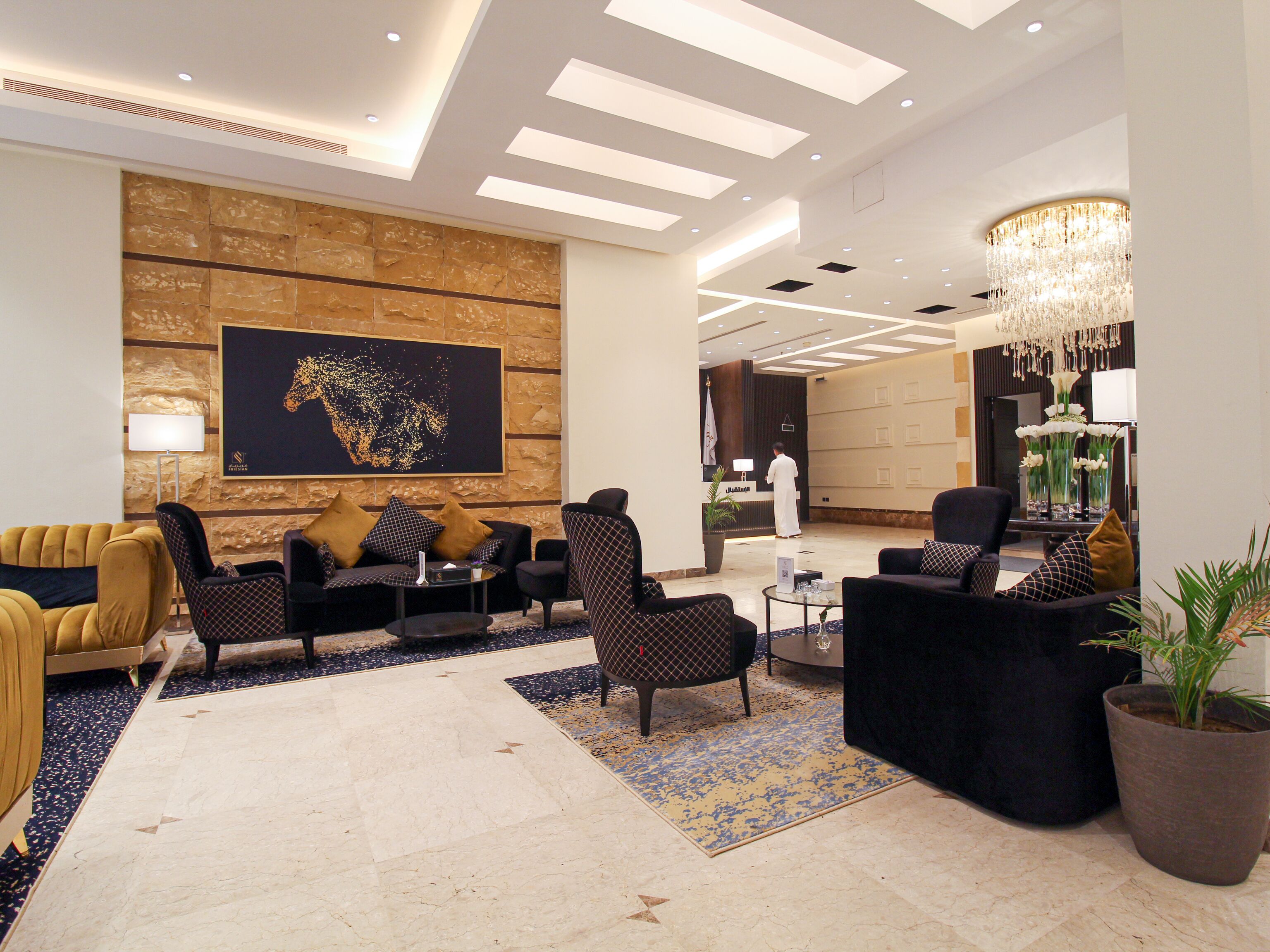 Een moderne lobby met een groot abstract kunstwerk, comfortabele zitplaatsen, een kroonluchter en een receptiebalie.