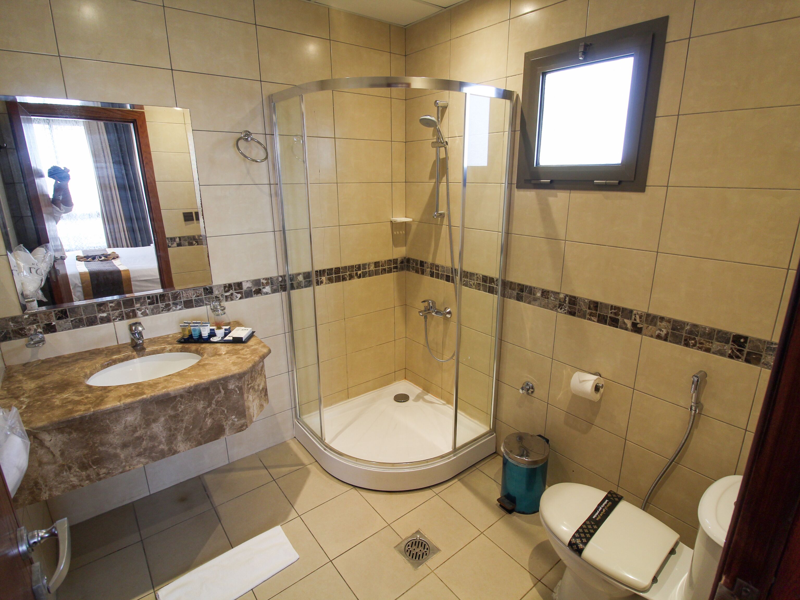 Un baño con ducha envuelta en vidrio, lavamanos con encimera de mármol y retrete.