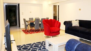 Una sala moderna con un televisor de pantalla plana, un sillón rojo, un sofá negro y una zona de comedor con una mesa y sillas.