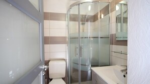 Uma casa de banho moderna com chuveiro em cabine de vidro, sanita branca e uma banheira grande.