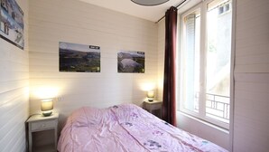 Um quarto com uma cama, duas mesas de cabeceira, uma janela com cortinas e dois posters de paisagens na parede.