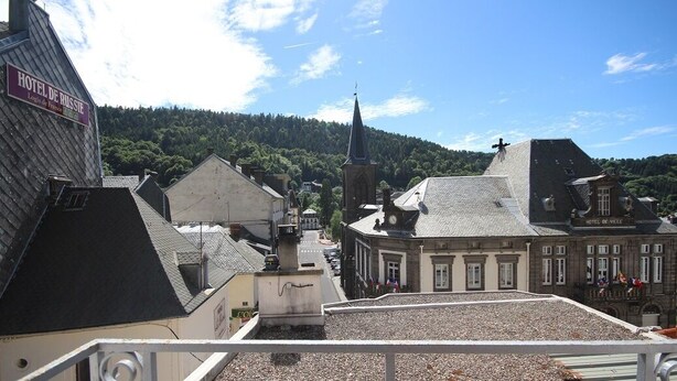Hotel de Ville com uma torre imponente e o topo de uma igreja ao fundo.