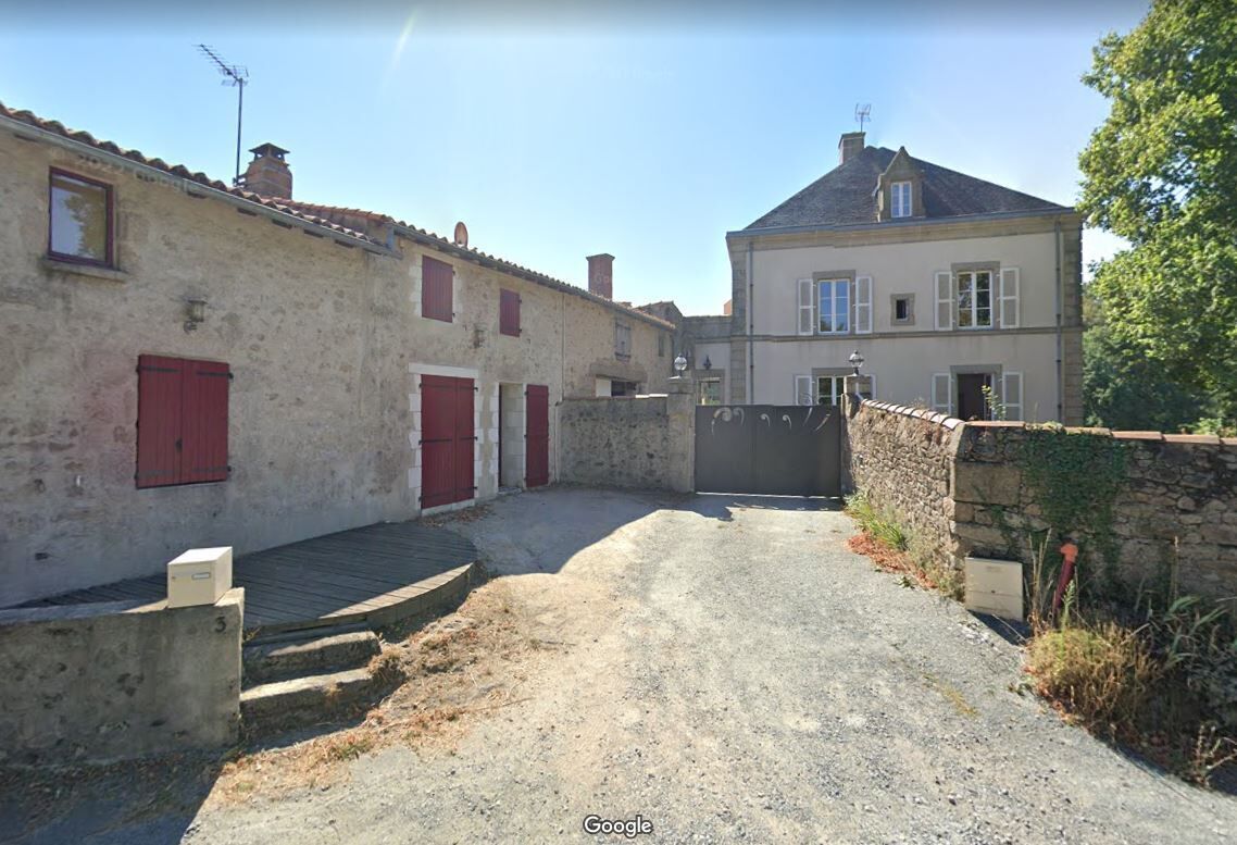 A narrow alleyway with a stone wall on one side and a building with red shutters on the other.