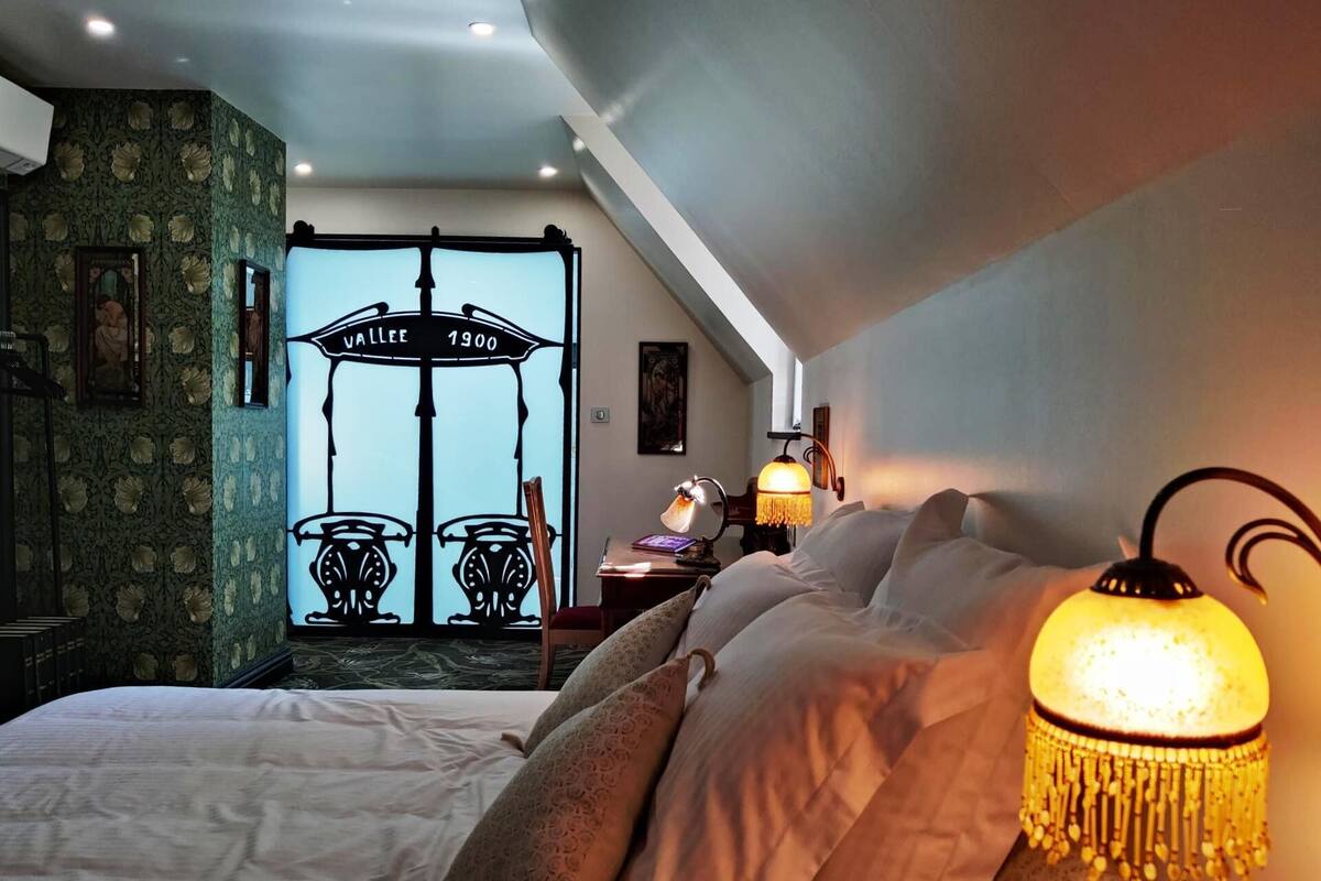 A bedroom with a bed, a desk with a lamp, a wall-mounted TV, and a decorative light fixture.
