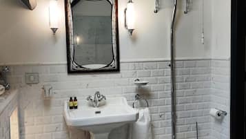 A bathroom with a white pedestal sink, a black toilet, a white toilet paper holder, a white trash can, and a mirror with a black frame.
