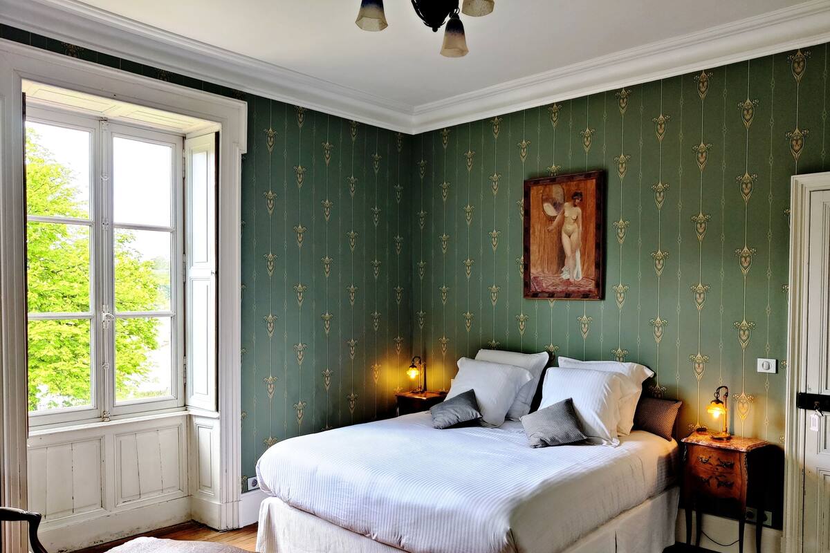 A bedroom with a large bed, a window, and a painting on the wall.
