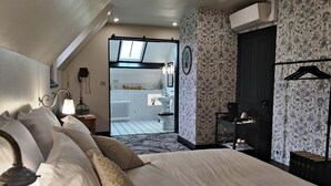Une chambre avec un grand lit, une table de chevet avec une lampe, une armoire et une salle de bain visible à travers une porte ouverte.