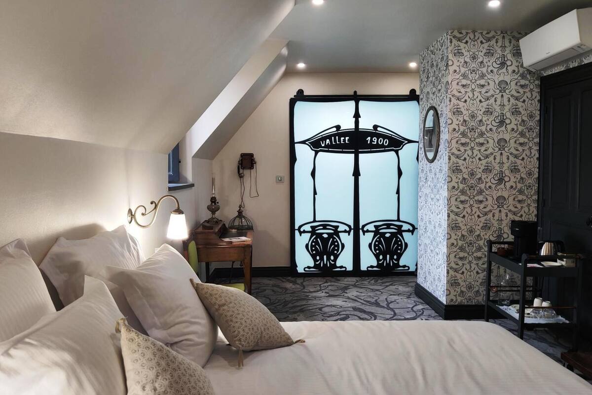 A hotel room with a bed, a desk, a chair, a lamp, and a door with a vintage design.