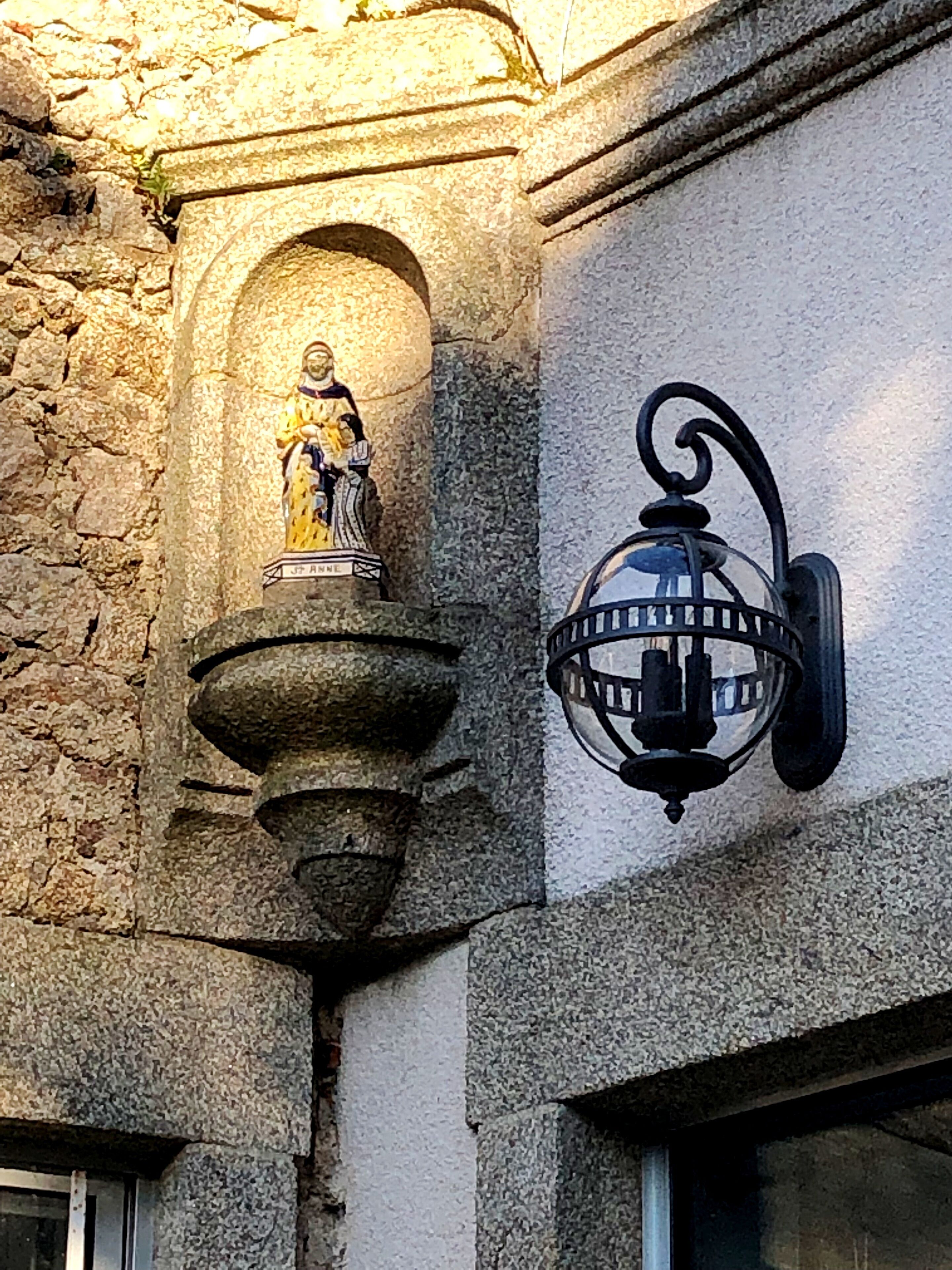 Un mur de pierre orné d’une statue et d’une lanterne.