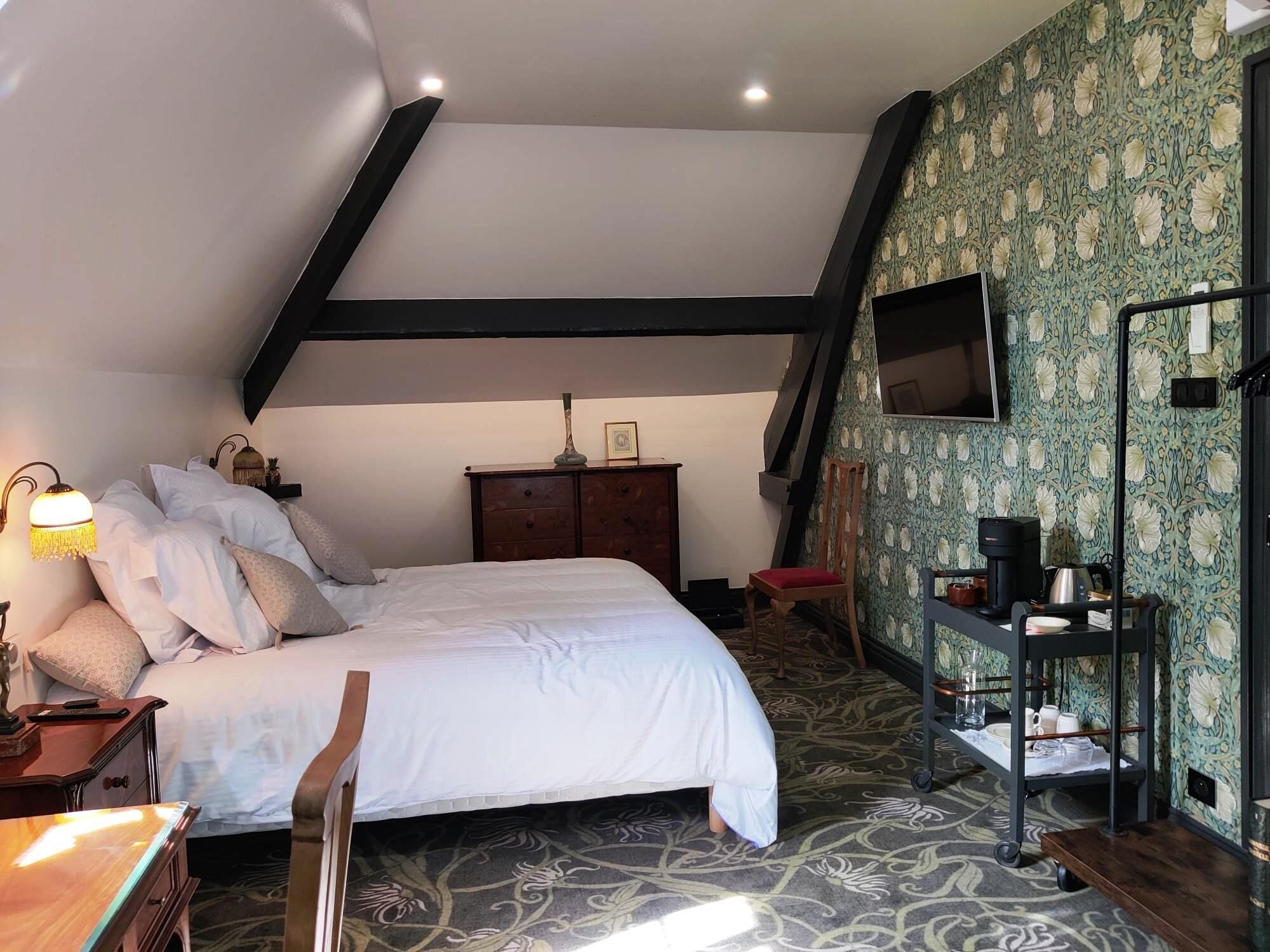 Un dormitorio con cama, mesita de noche, cómoda, silla, escritorio, estante y televisor.