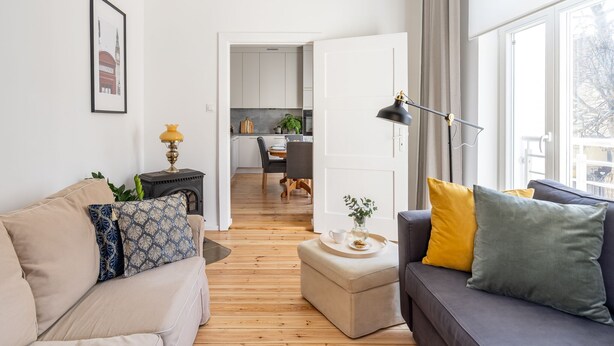 A modern living room with a sofa, ottoman, and a dining area in the background. - London - Cozy City Stay by Lion Apartments Sopot (Sopot)