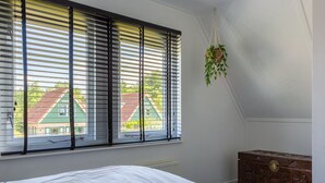Un dormitorio con cama, cómoda, ventana con persianas y planta colgante.