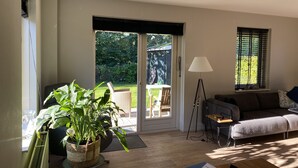 Una sala de estar con puerta corrediza de vidrio que da a un jardín, un sofá, una lámpara de pie y una planta en maceta.