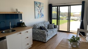A modern kitchen with a built-in sink, a dining area with a table and chairs, a patterned sofa, and a large sliding glass door leading to a patio. - Entire 1br 50sm guest suite 3mins to beach shops restaurants small dog welcome.
 (Ulladulla)