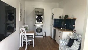 A compact kitchen with a built-in washing machine, a dining area with a chair, and a sofa with patterned cushions. - Entire 1br 50sm guest suite 3mins to beach shops restaurants small dog welcome.
 (Ulladulla)