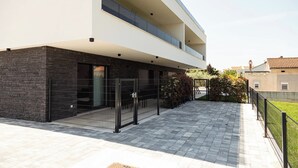 Un edificio moderno de dos pisos con fachada de piedra, entrada porticada y patio empedrado.